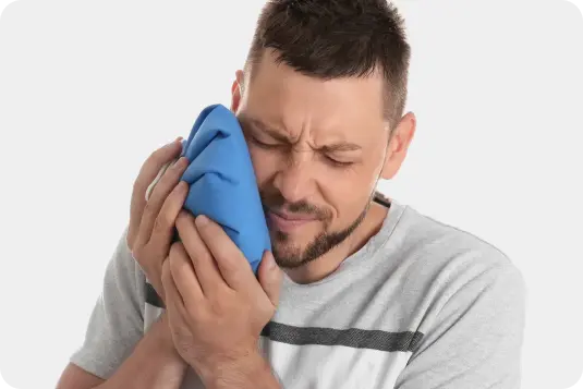 Vīrietis ar aizvērtām acīm tur aukstuma kompresi pie vaiga, ar diskomfortu žokļa vai zoba sāpēm