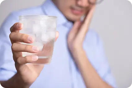 Vīrietis tur glāzi ūdens ar ledu un tur roku pie vaiga no zobu sāpem izraisīta no aukstuma