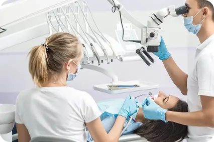 Zobārsts mikroskopā veic saknes kanāla ārstēšanu pacientei zobārstniecības kabinetā