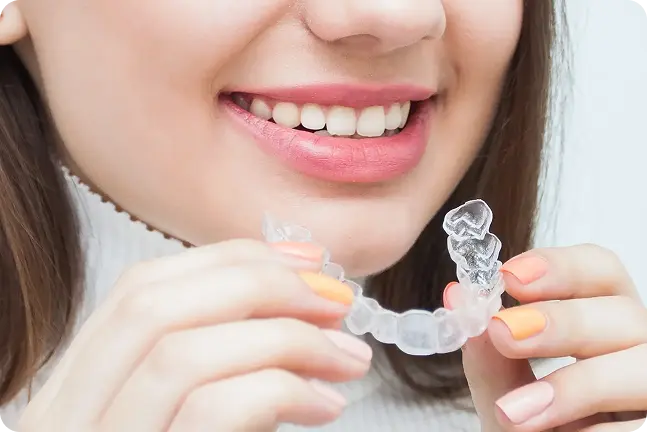 Sieviete smaida un rokās tur caurspīdīgās kapes zobu taisnošanai